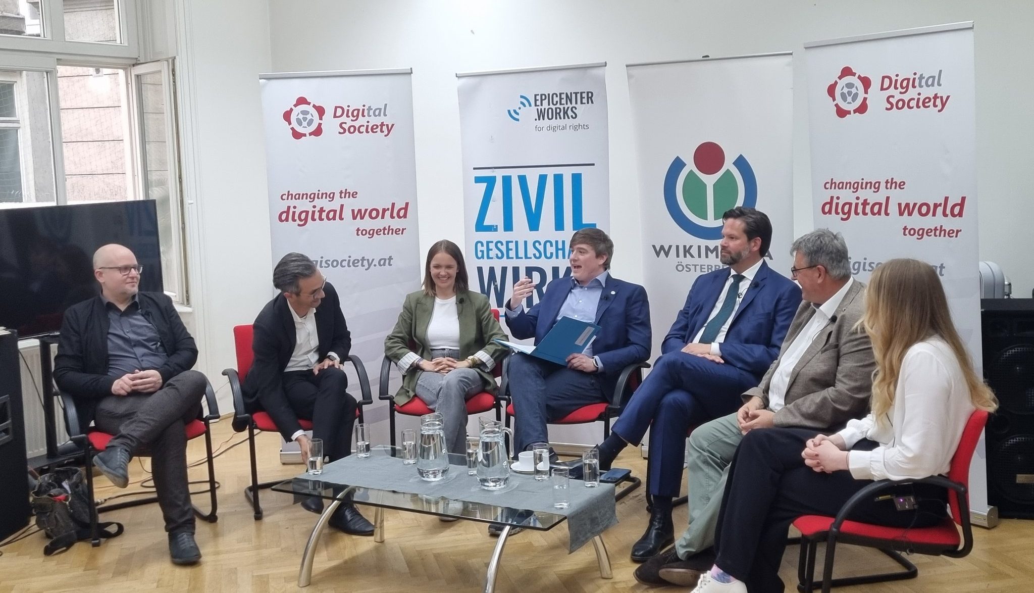 GOMkmc2W4AEiN3d Foto der Diskutierenden im Halbkreis sitzend vor den Roll-Ups von Digital Society, epicenter.works und Wikimedia Österreich